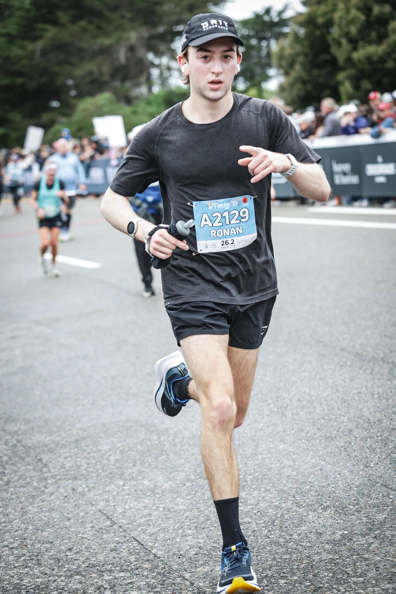 Ronan running toward the camera between crowd barriers lined with spectators, bib A2129 on his black T-shirt.